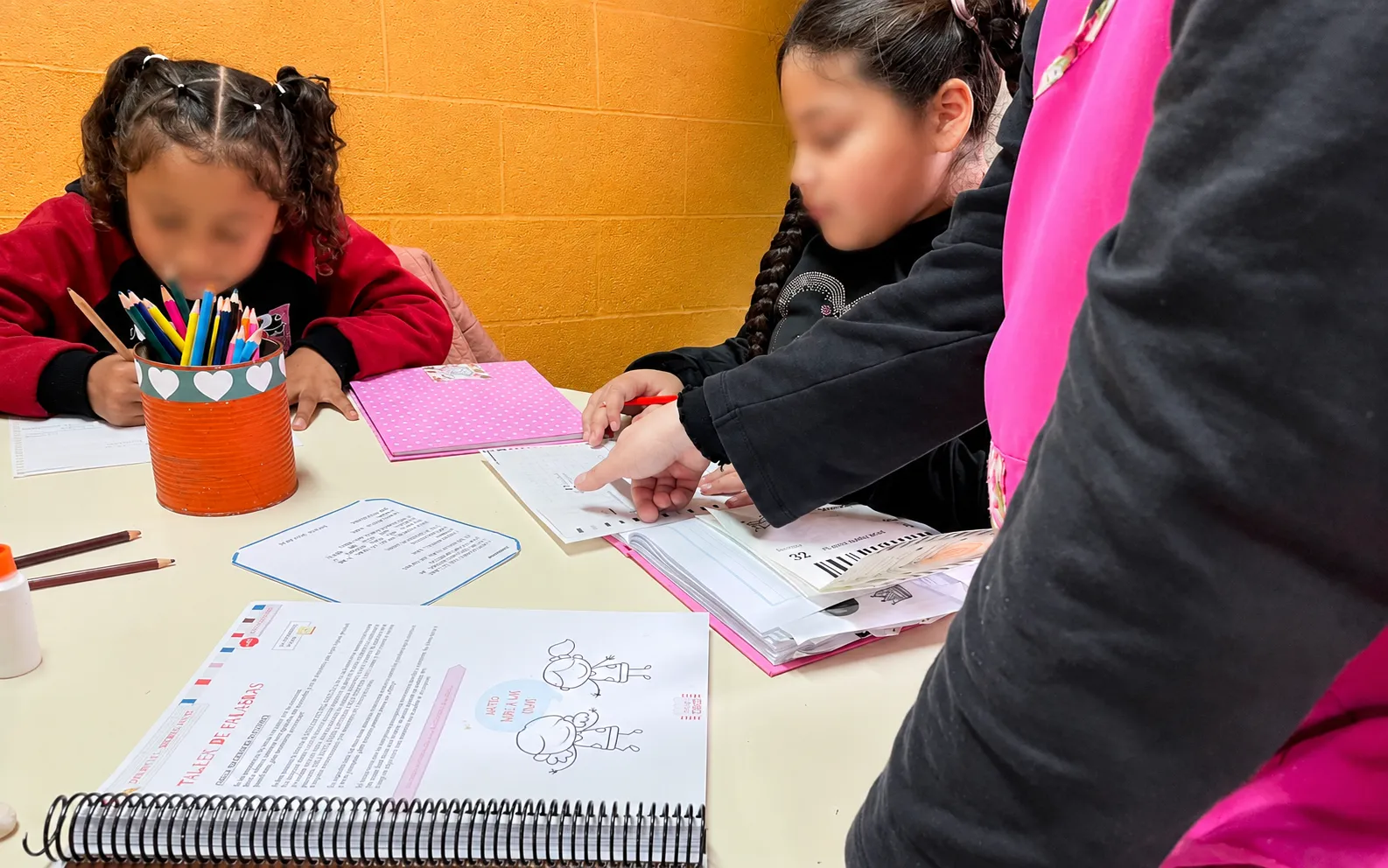 Una docente acompaña a una alumna señalando una consigna en el libro