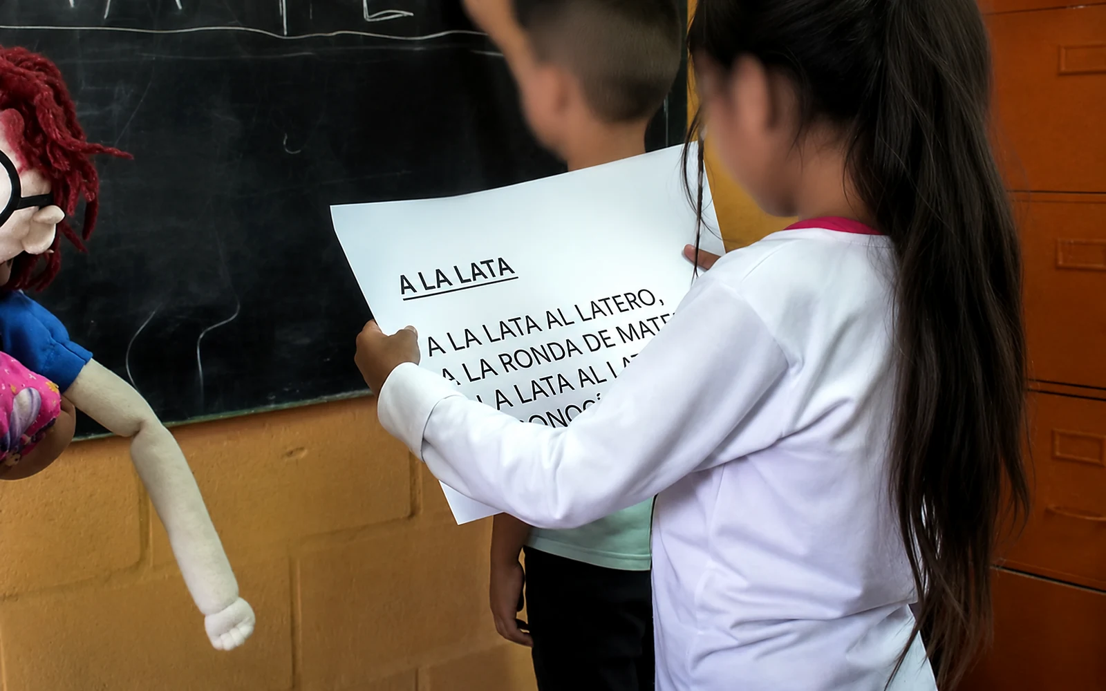 Dos chicos sostienen frente al pizarrón una lámina con un texto para leer en voz alta