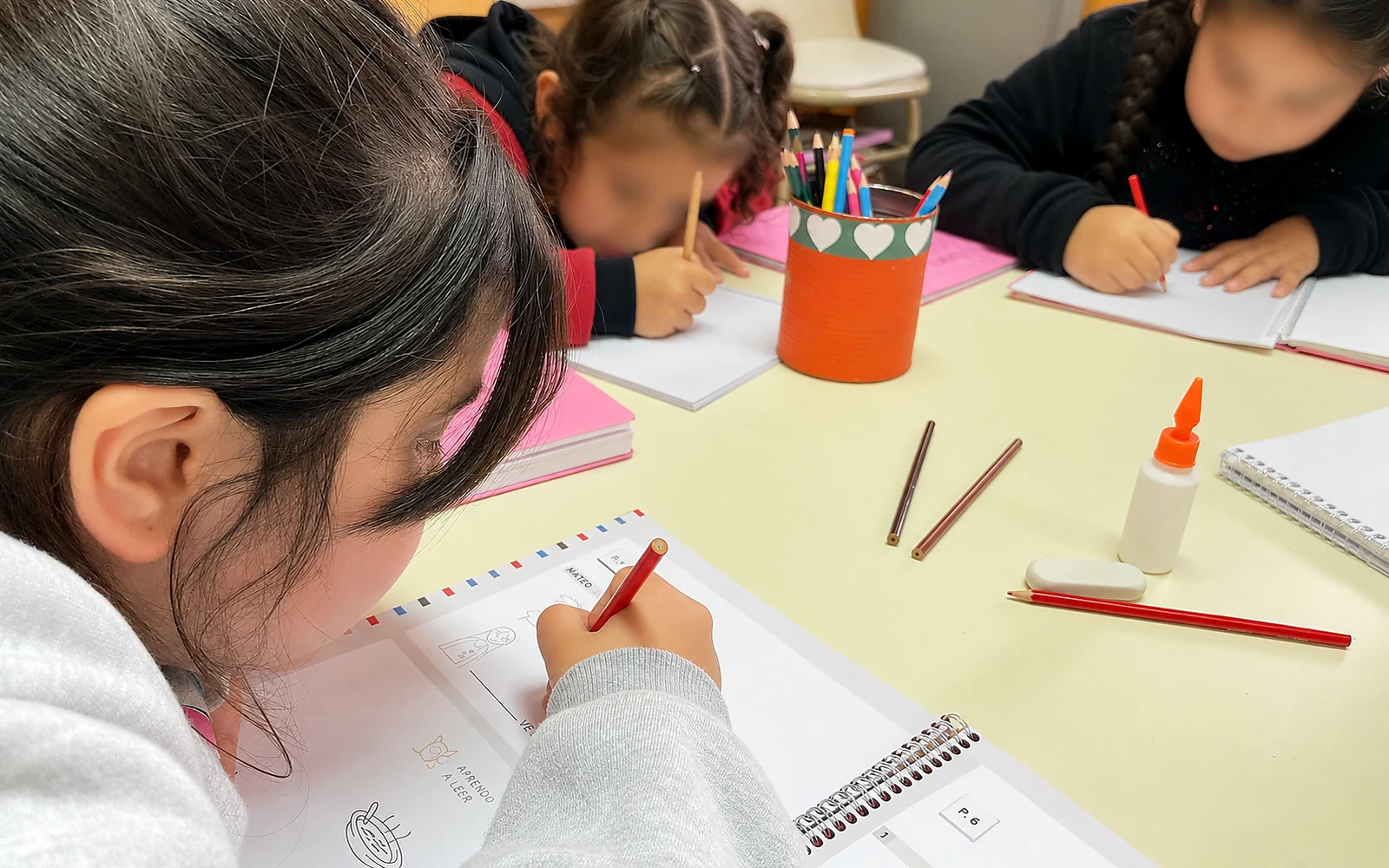 Chicos trabajando en grupo alrededor de la mesa con sus libros y lápices